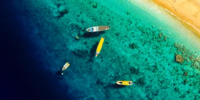 Vista aérea de barcos em águas costeiras turquesa junto a uma praia de areia