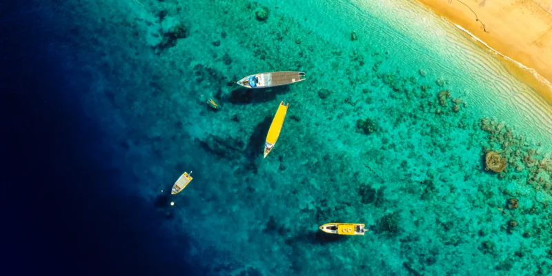 Vista aérea de barcos em águas costeiras turquesa junto a uma praia de areia