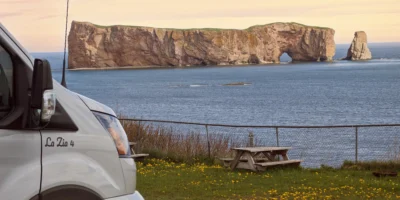 Van de camping e mesa de piquenique na costa com vista para o rochedo Percé, em Québec