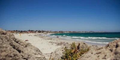 Banhistas e ondas em Sorrento Beach, com rochas em primeiro plano