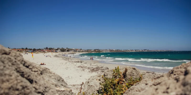 Banhistas e ondas em Sorrento Beach, com rochas em primeiro plano