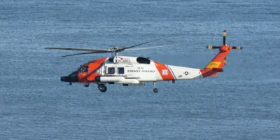Helicóptero branco e laranja da Guarda Costeira dos Estados Unidos a voar sobre o mar azul. Fotografia ilustrativa de arquivo de 2021; não mostra o resgate ao largo de Ensenada em outubro de 2026.